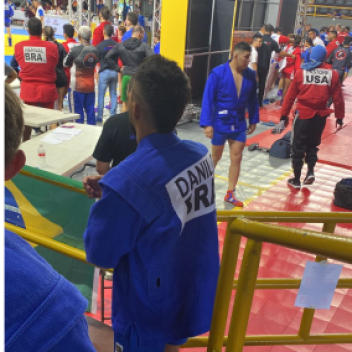 Atleta brasileiro de quimono azul, de costas, observa a área de aquecimento de uma competição de SAMBO