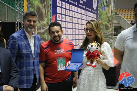 Virginia Mendes recebe o mascote do SAMBO e uma caixa com bótons das mãos de dirigentes no Pan-Americano 2024