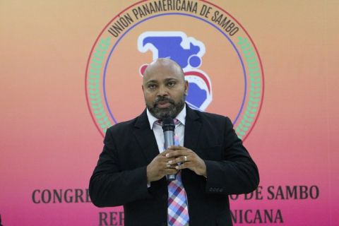 Eliseo Romero discursa ao microfone diante do logo da União Pan-Americana de Sambo